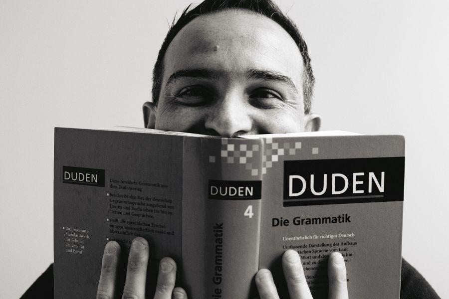 die deutSCHule; Lehrer Porträt Marco versteckt sich hinter einem Grammatik-Buch